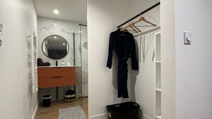Ein Korridor mit Holzboden, einem Spiegel, einem schwarzen Bademantel an einem Gestell, einem schwarzen Korb und einer weißen Wand mit Lichtschalter.