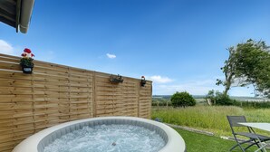 Ein Whirlpool, umgeben von einem Holzzaun, ein Tisch mit Stühlen und Blick auf die Landschaft.