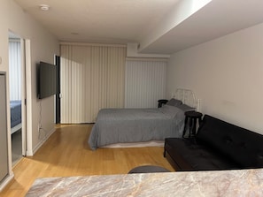 Ein Schlafzimmer mit einem Bett, einer schwarzen Couch, einem Fernseher und einem Fenster mit Jalousien.