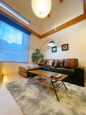 A living room with a sofa, a coffee table, a lamp, and a large window. - 4 min. walk from station, 10 min. from USJ, 10 min. from Nara-Kobe-Namba-Dotonbori 1 train line, 10 min. from Umeda train line, luxury bath and kitchen, MAX 6 people, Mario kids room, Tatami room, 1 building for rent (大阪市此花区 梅香)