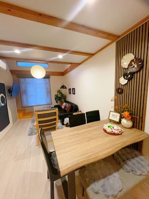 A dining area with a wooden table, chairs, a vase with flowers, and a wall-mounted clock. - 4 min. walk from station, 10 min. from USJ, 10 min. from Nara-Kobe-Namba-Dotonbori 1 train line, 10 min. from Umeda train line, luxury bath and kitchen, MAX 6 people, Mario kids room, Tatami room, 1 building for rent (大阪市此花区 梅香)