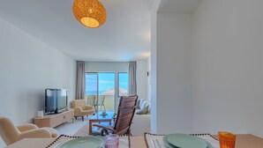 Een hotelkamer met een eettafel gedekt voor twee personen, een televisie, een bank en een balkon met uitzicht.