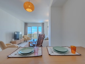 A hotel room with a dining table set for two, a television, a sofa, and a balcony with a view. - Algarvemor - Casa Do Tio by Interhome (Portimão)