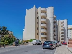 Un immeuble résidentiel à plusieurs étages, doté de balcons, avec des voitures garées devant et un ciel bleu dégagé.