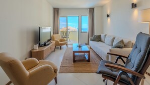Een moderne woonkamer met een televisie, bank, stoelen en uitzicht op zee.