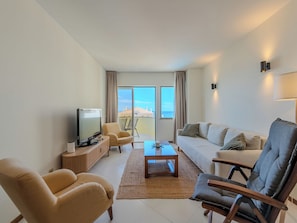A modern living room with a television, sofa, chairs, and a view of the sea. - Algarvemor - Casa Do Tio by Interhome (Portimão)