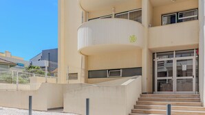 Een gebouw met een gebogen balkon, een trap naar de ingang en een betegeld voetpad.