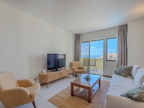 Un salon moderne avec un téléviseur, un canapé, des fauteuils et un balcon offrant une vue agréable.