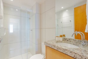 Ein modernes Badezimmer mit einer Duschkabine aus Glas, einem weißen Waschbecken mit Marmorplatte und einer Holzkommode.