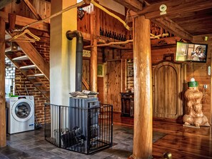 A rustic interior with a stone fireplace, wooden beams, a washing machine, and a television. - Chata Ujo by Interhome (Hranice)