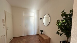 A hallway with a wooden bench, a potted plant, a round mirror on the wall, and a white door. - Faraway Homes Studios Krieglach 18 (Sommer)