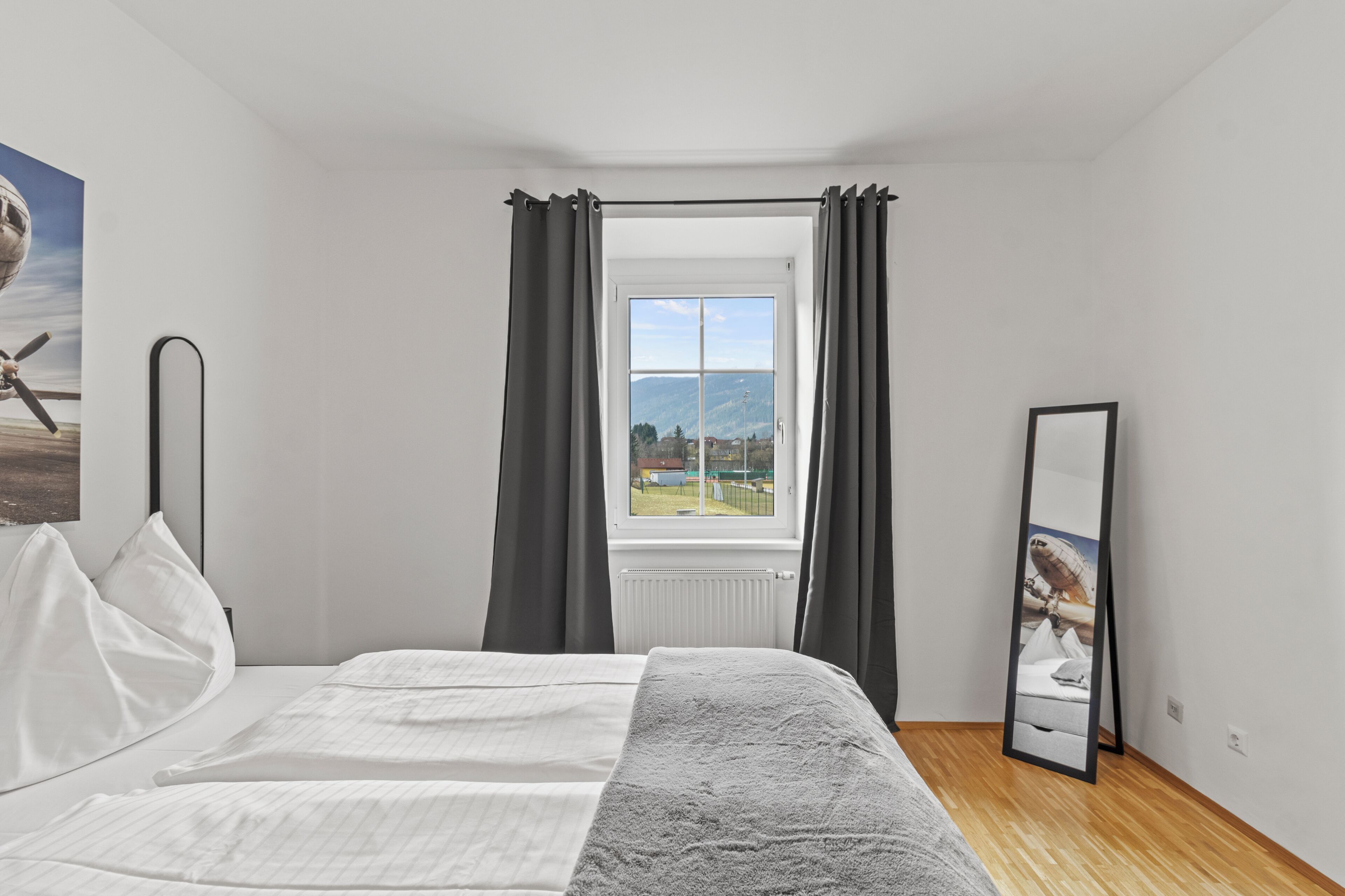 Een slaapkamer met een bed, een raam met gordijnen, een radiator en een spiegel.