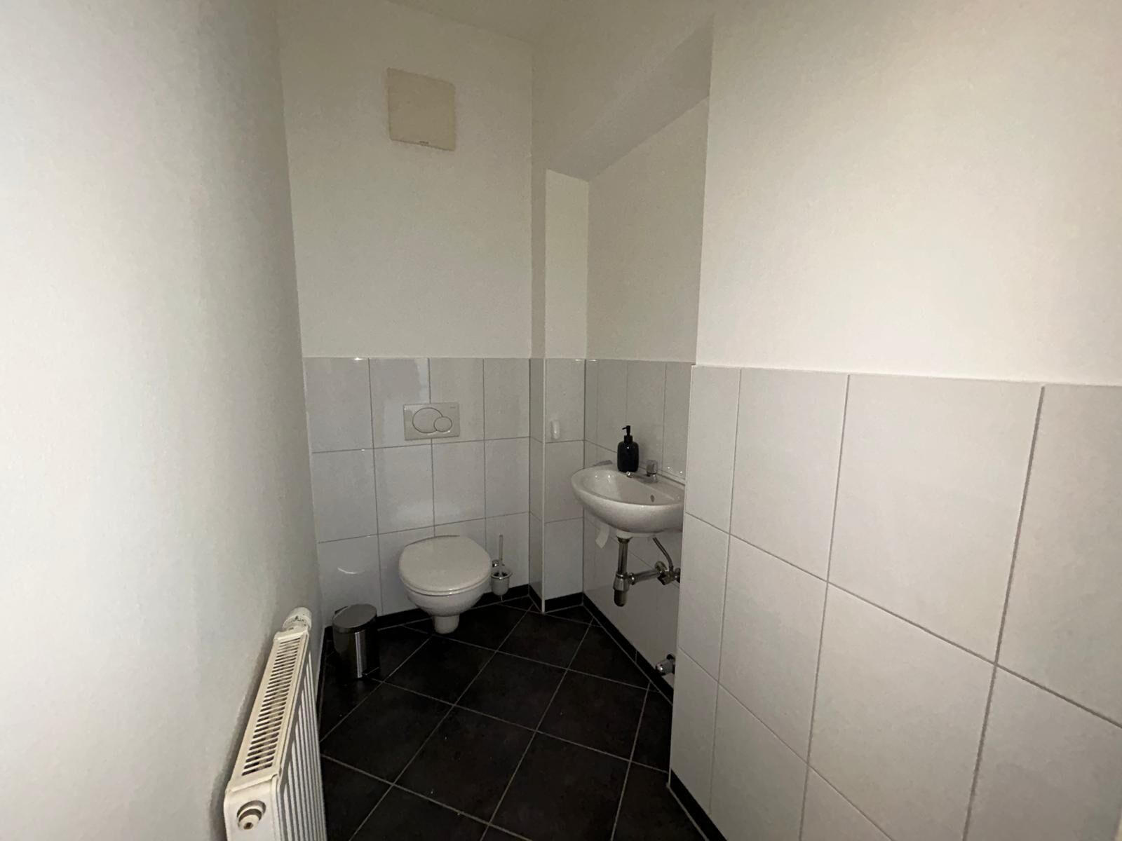 Une petite salle de bain étroite, équipée d’un WC, d’un lavabo et d’un radiateur.