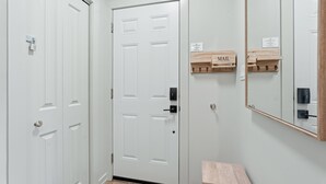 A hallway with white doors, a small wooden bench, and a mirror on the wall. - Cozy Cityscapes 3Br, 1B with Washer+Dryer (St. Catharines)