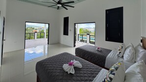 Een hotelkamer met twee bedden, een plafondventilator en een balkon met uitzicht.