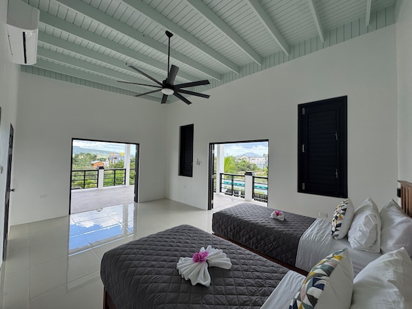 A hotel room with two beds, a ceiling fan, and large windows with a view of a pool and greenery.