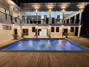 A modern building with a swimming pool, multiple balconies, and outdoor lighting.