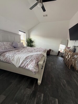 Ein Schlafzimmer mit Bett, Deckenventilator, Nachttisch, Spiegel und an der Wand montiertem Fernseher.