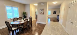 A dining area with a wooden table and chairs, a potted plant, and a kitchen in the background.
