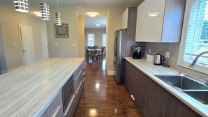 A modern kitchen with a long countertop, stainless steel appliances, and pendant lighting.