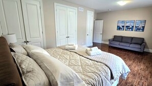 A bedroom with a large bed, two doors, a gray sofa, and three wall-mounted paintings.