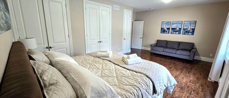 A bedroom with a large bed, two doors, a gray sofa, and three wall-mounted paintings.