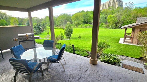 A covered patio with a grill, a glass table, and blue chairs.