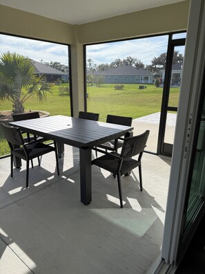 Ein überdachter Patio-Bereich mit Tisch und Stühlen, einer Palme und Blick auf eine Wohngegend.