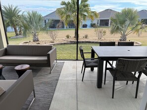 A patio area with a sofa, dining table, chairs, and a view of a residential neighborhood.