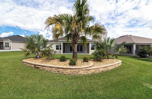 Una propiedad residencial con un césped bien cuidado, una palmera y un jardín circular de ladrillo.