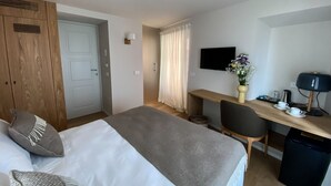 A hotel room with a bed, a desk, a chair, a TV, and a small table with a vase of flowers. - La Torre Belgirate - Luxury Rooms - Camelia - By Guestaly (Belgirate)