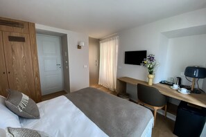A hotel room with a bed, a desk, a chair, a TV, and a small table with a vase of flowers.