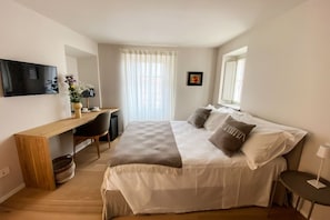 A bedroom with a bed, a desk, a chair, a TV, and a window with curtains.