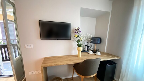 A modern room with a wooden desk, a flat-screen TV, a chair, a small trash bin, and a vase with flowers. - La Torre Belgirate - Luxury Rooms - Camelia - By Guestaly (Belgirate)
