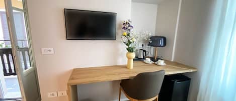 A modern room with a wooden desk, a flat-screen TV, a chair, a small trash bin, and a vase with flowers.