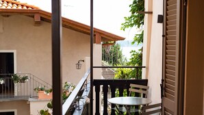 A balcony with a table and chairs, potted plants, and a view of a building with a tiled roof. - La Torre Belgirate - Luxury Rooms - Camelia - By Guestaly (Belgirate)