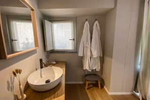 Ein Badezimmer mit einem großen weißen Waschbecken, einem Spiegel, einem Fenster und zwei weißen Bademänteln, die an der Wand hängen.