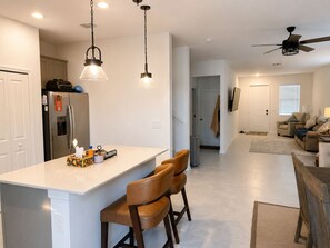 Eine moderne Küche mit Kochinsel, Barhocker, Kühlschrank und Pendelleuchten.