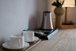 Una bandeja con dos tazas blancas sobre una mesa de madera, una cafetera y una lámpara al fondo.