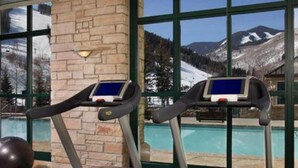 Dos cintas de correr con pantallas digitales, un pilar de piedra y vistas de un paisaje montañoso a través de amplios ventanales.