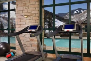 Two treadmills with digital displays, a stone pillar, and a view of a mountain landscape through large windows. - 2-bedroom residence in luxury resort with spa & nightly turn down service (Avon)
