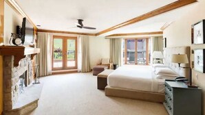 Habitación de hotel con una cama grande, un escritorio, una silla, un aparador, un ventilador de techo y vistas al exterior a través de las ventanas.