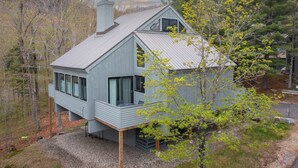 Ein modernes Haus mit einer großen Terrasse, einem Schornstein und Blick auf den umliegenden Wald.