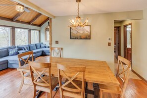 A dining area with a wooden table and chairs, a chandelier, a large window, and a stone wall.