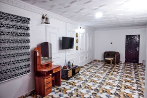 Una stanza con parete decorata, televisione a schermo piatto, comò in legno, un piccolo tavolo rotondo e pavimento a motivi.