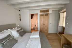 Une chambre à coucher avec un lit, des tables de chevet, une armoire et une salle de bain visible à travers une porte ouverte.