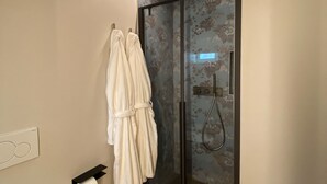Ein Badezimmer mit Duschkabine aus Glas, einem Handtuchhalter mit zwei weißen Handtüchern und einem Toilettenpapierhalter.