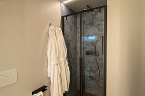 A bathroom with a glass shower enclosure, a towel rack with two white towels, and a toilet paper holder.