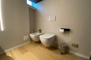 Une salle de bain moderne équipée d’un bidet, de toilettes et d’une poubelle.