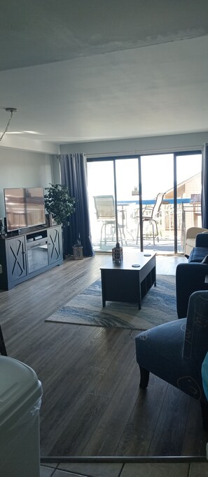 A spacious living area with a large window, a flat-screen TV, a coffee table, and a sofa. - Forest Dunes 508 - Oceanfront Condo with Community Pools! (Myrtle Beach)